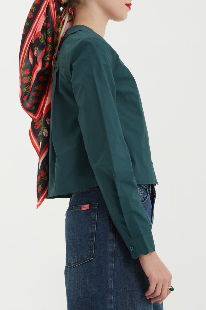 Camisa verde de poplin de largo hasta la cadera con terminación en forma de onditas en cuello, puños y cartera y botones a tono en forma de flor. 
