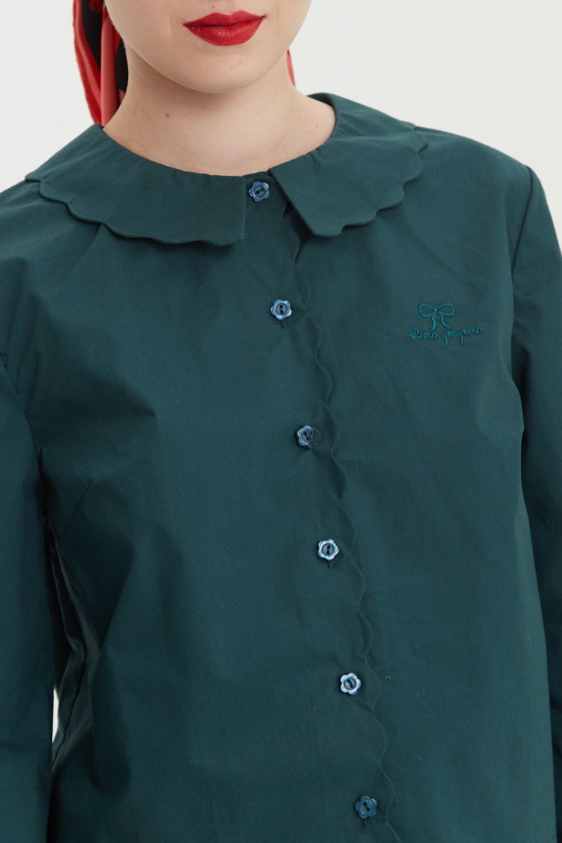 Camisa verde de poplin de largo hasta la cadera con terminación en forma de onditas en cuello, puños y cartera y botones a tono en forma de flor. 