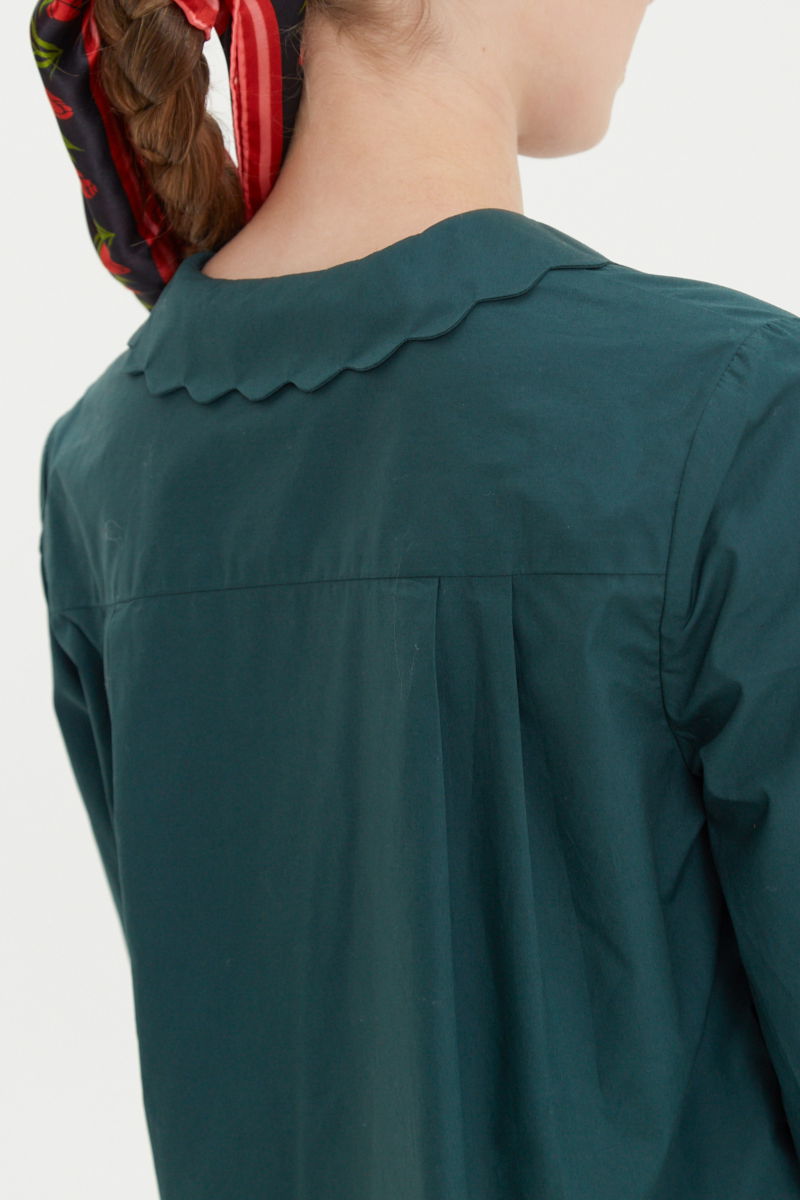 Camisa verde de poplin de largo hasta la cadera con terminación en forma de onditas en cuello, puños y cartera y botones a tono en forma de flor. 