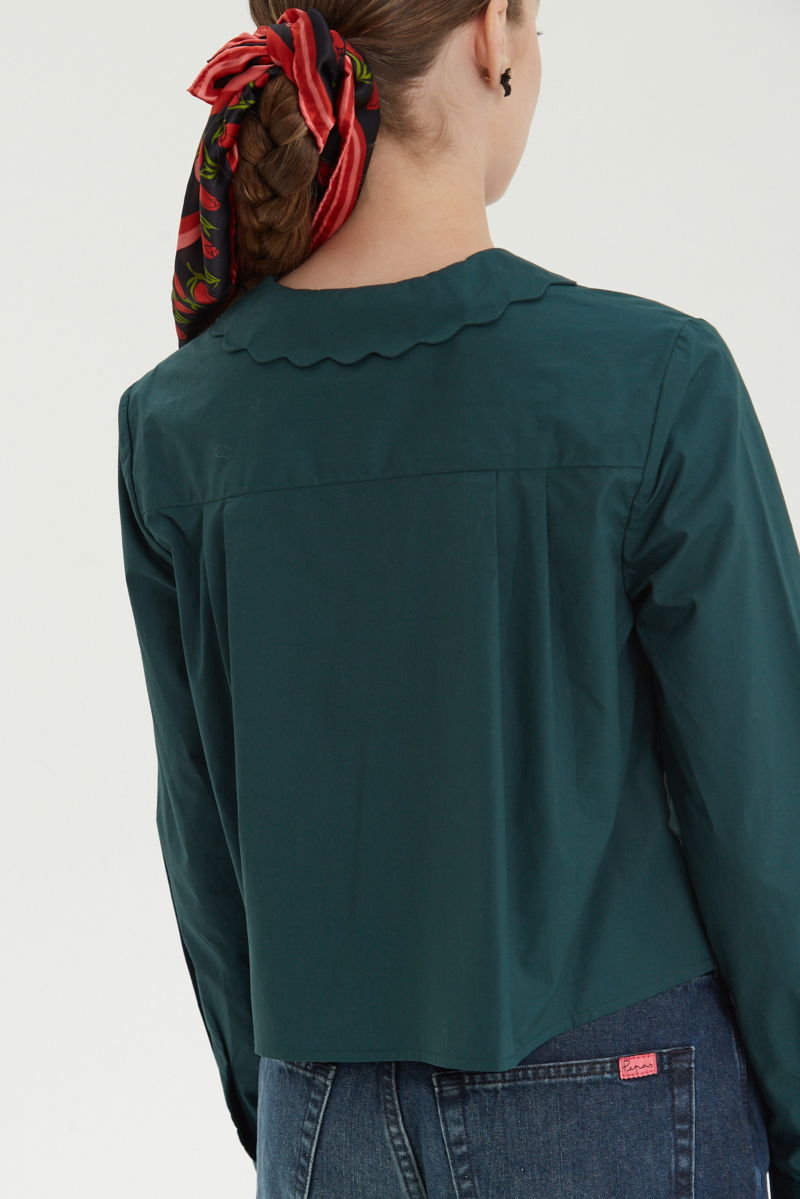 Camisa verde de poplin de largo hasta la cadera con terminación en forma de onditas en cuello, puños y cartera y botones a tono en forma de flor. 