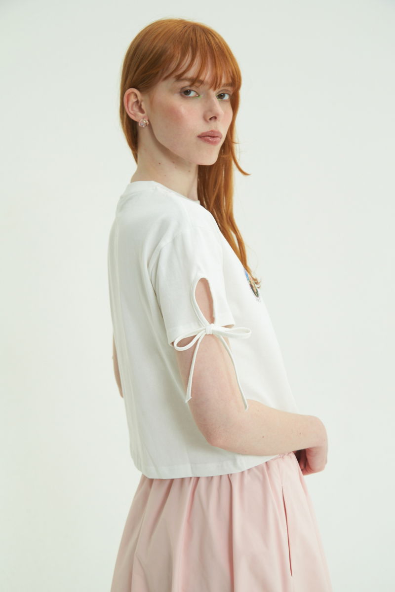 Remera blanca suelta y crop de algodón estampada con lazos en las mangas para atar en moño.
