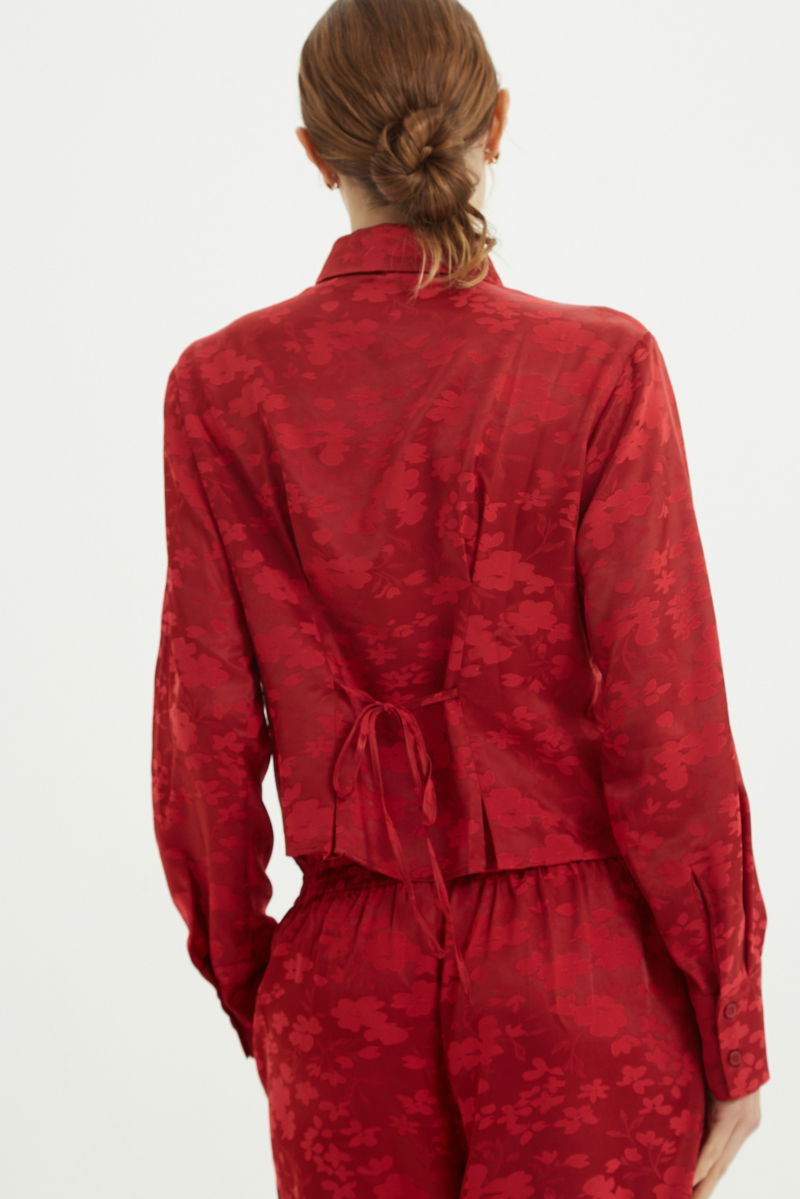 Camisa roja satinada de jacquard floreado con pinzas de entalle en frente y espalda, con lazo para regular. 