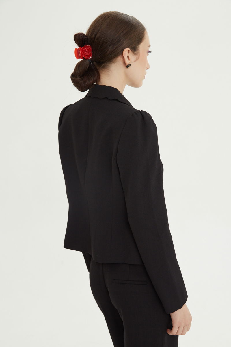 Blazer negro sastrero entallado con terminación ondulada y mangas princesa. 
