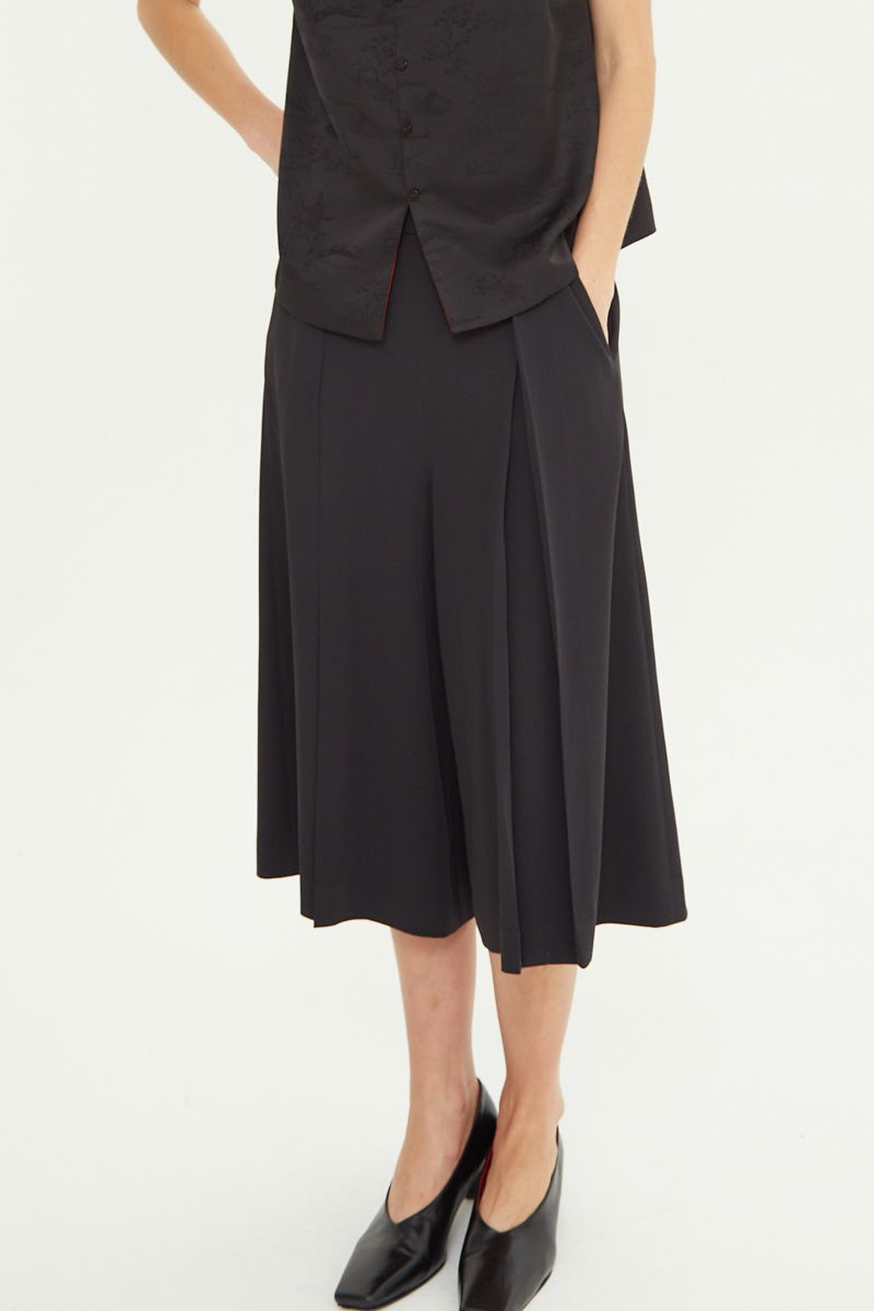 Bermuda negra sastrera tiro medio con piernas anchas hasta la rodilla, cintura trasera con elástico, tablas y bolsillos laterales. 