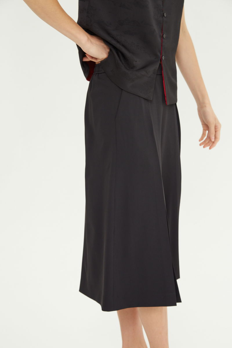 Bermuda negra sastrera tiro medio con piernas anchas hasta la rodilla, cintura trasera con elástico, tablas y bolsillos laterales. 