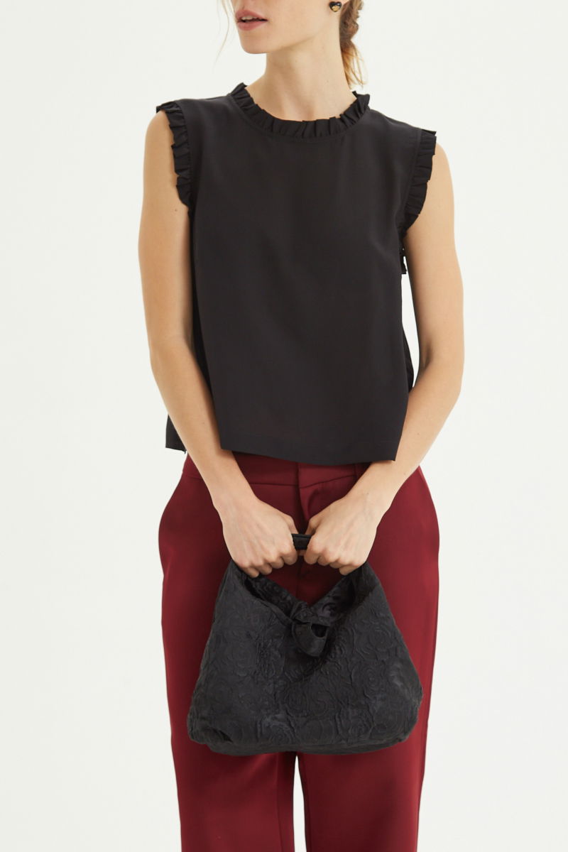 Musculosa negra de seda con volados en cuello y sisas, de corte recto y larga a la cadera con cuello mao y botones en la espalda. 
