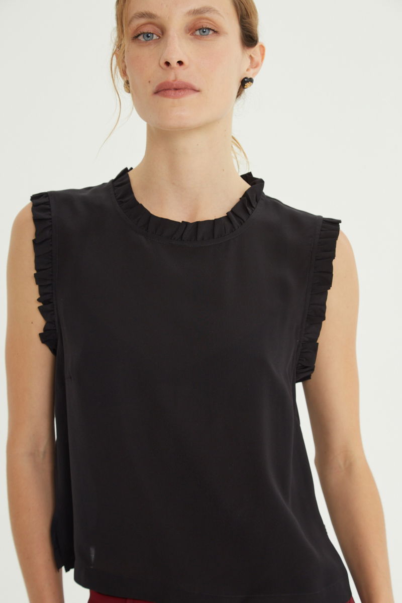 Musculosa negra de seda con volados en cuello y sisas, de corte recto y larga a la cadera con cuello mao y botones en la espalda. 
