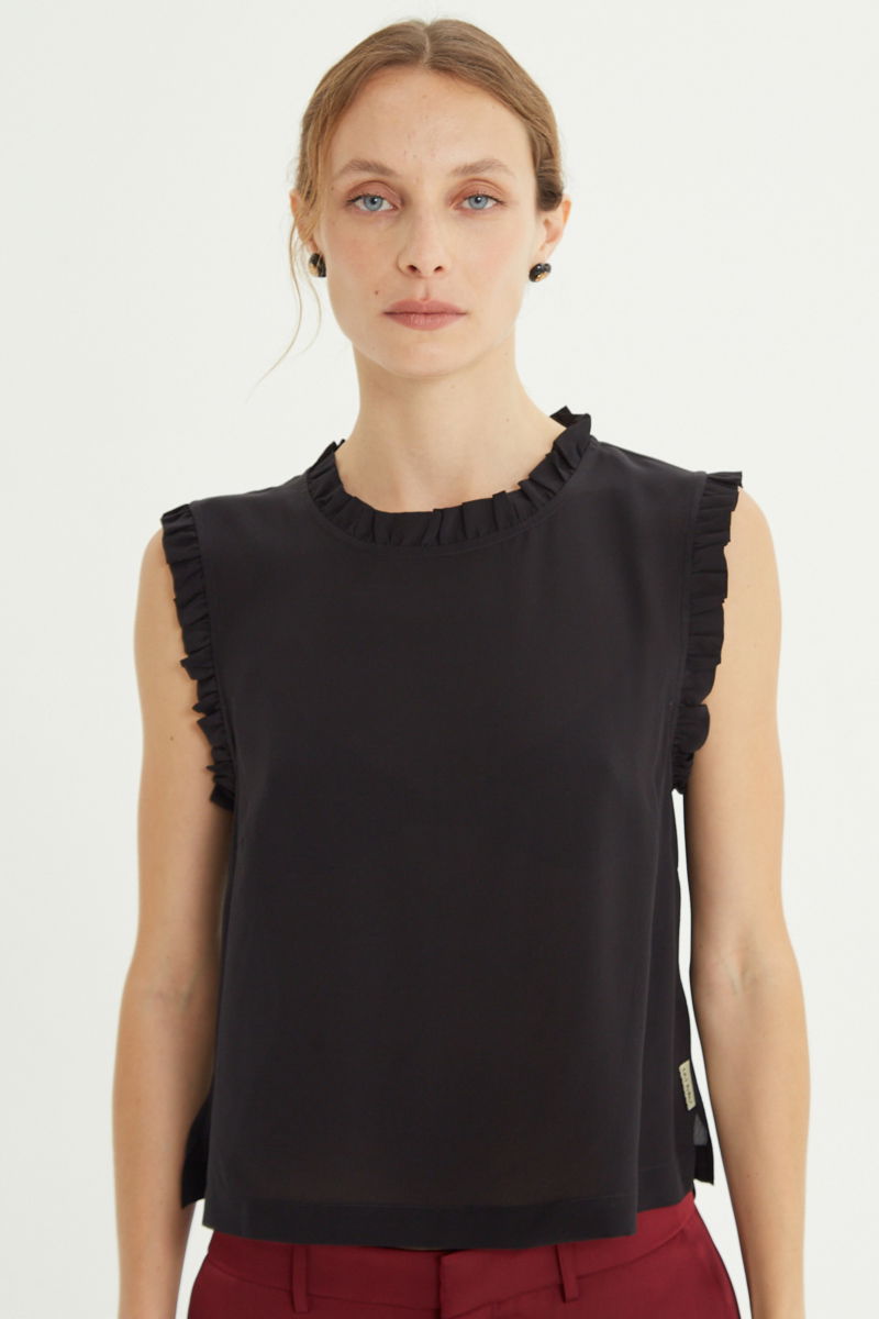 Musculosa negra de seda con volados en cuello y sisas, de corte recto y larga a la cadera con cuello mao y botones en la espalda. 
