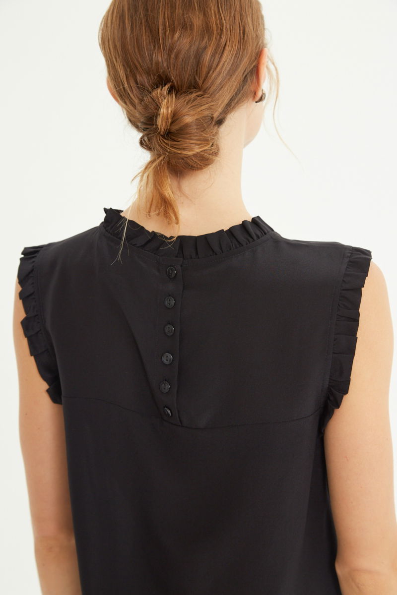 Musculosa negra de seda con volados en cuello y sisas, de corte recto y larga a la cadera con cuello mao y botones en la espalda. 
