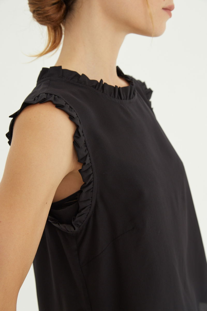 Musculosa negra de seda con volados en cuello y sisas, de corte recto y larga a la cadera con cuello mao y botones en la espalda. 
