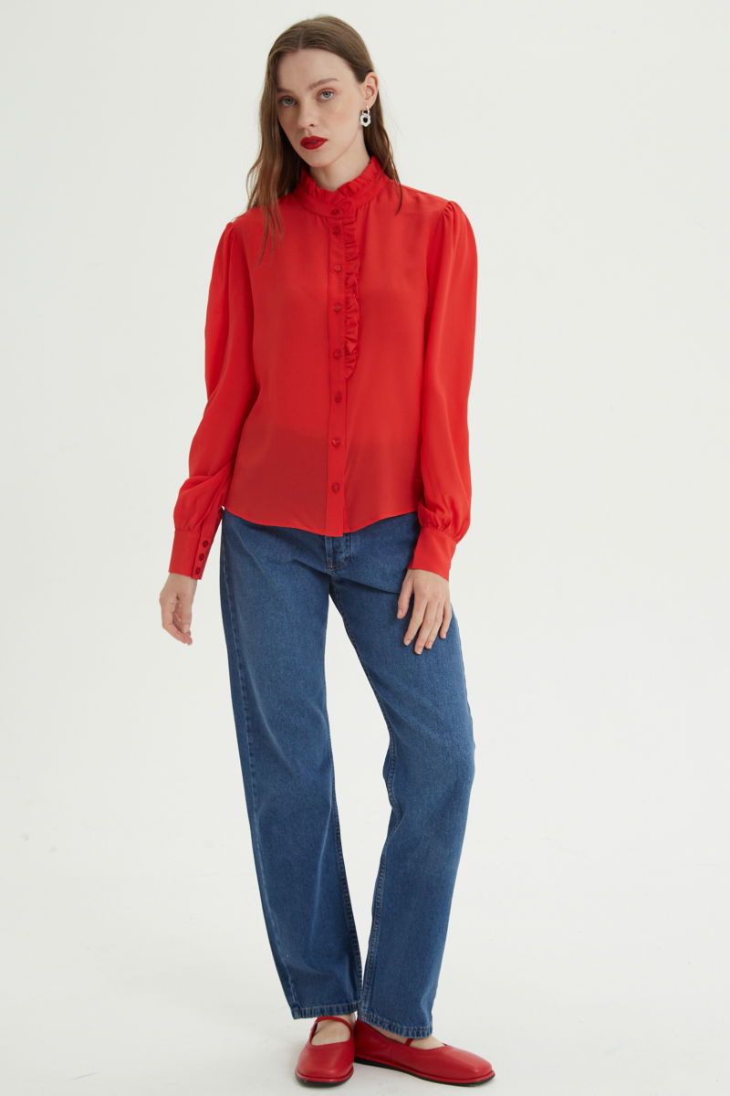 Camisa roja de seda recta y larga a la cadera con cuello mao y volados en el cuello y la cartera, con frunces en los hombros y puños y botones a tono. 