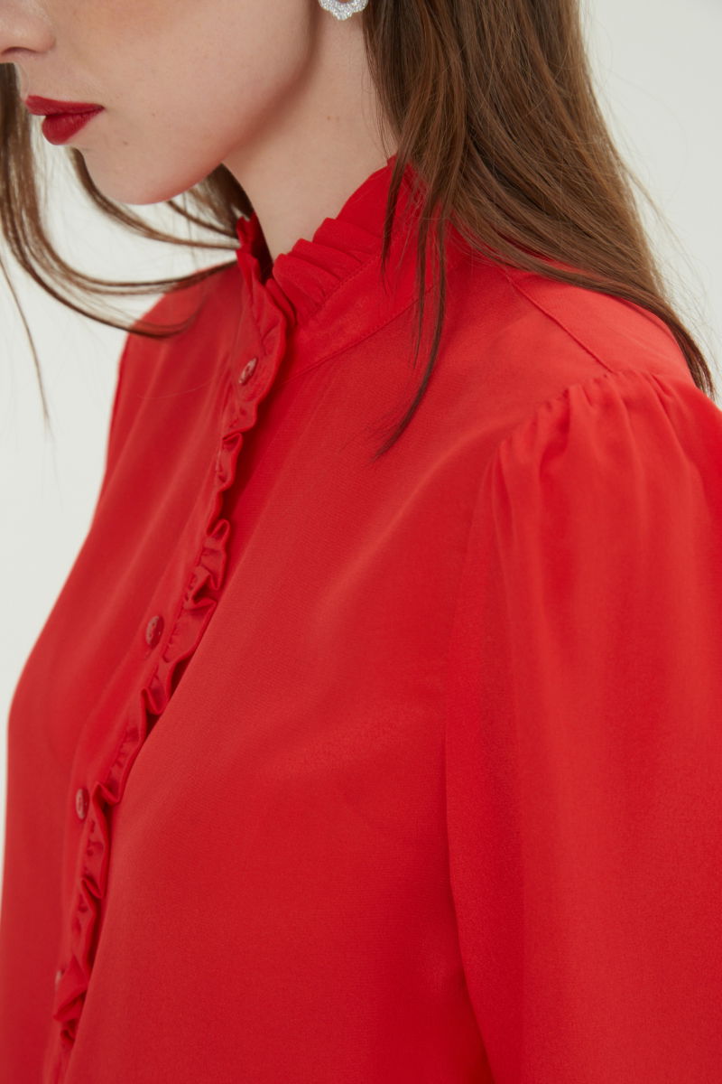 Camisa roja de seda recta y larga a la cadera con cuello mao y volados en el cuello y la cartera, con frunces en los hombros y puños y botones a tono. 