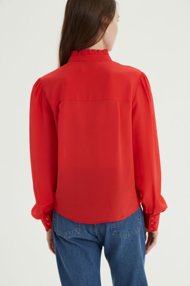 Camisa roja de seda recta y larga a la cadera con cuello mao y volados en el cuello y la cartera, con frunces en los hombros y puños y botones a tono. 