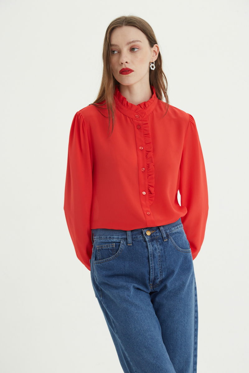 Camisa roja de seda recta y larga a la cadera con cuello mao y volados en el cuello y la cartera, con frunces en los hombros y puños y botones a tono. 