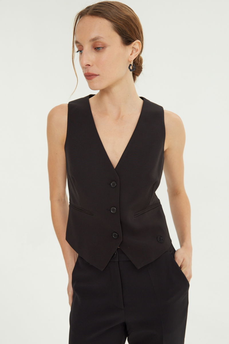 Chaleco negro sastrero largo a la cadera con botones a tono, bolsillos ojal y pinzas en frente y espalda. 
