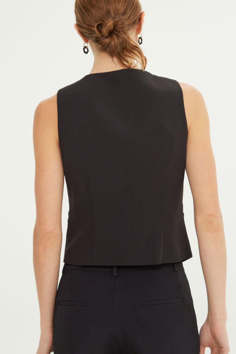 Chaleco negro sastrero largo a la cadera con botones a tono, bolsillos ojal y pinzas en frente y espalda. 
