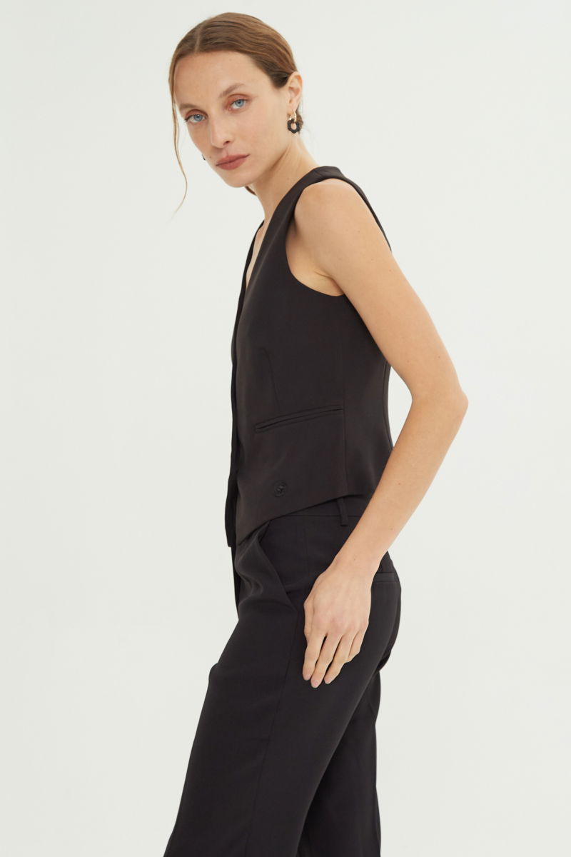 Chaleco negro sastrero largo a la cadera con botones a tono, bolsillos ojal y pinzas en frente y espalda. 
