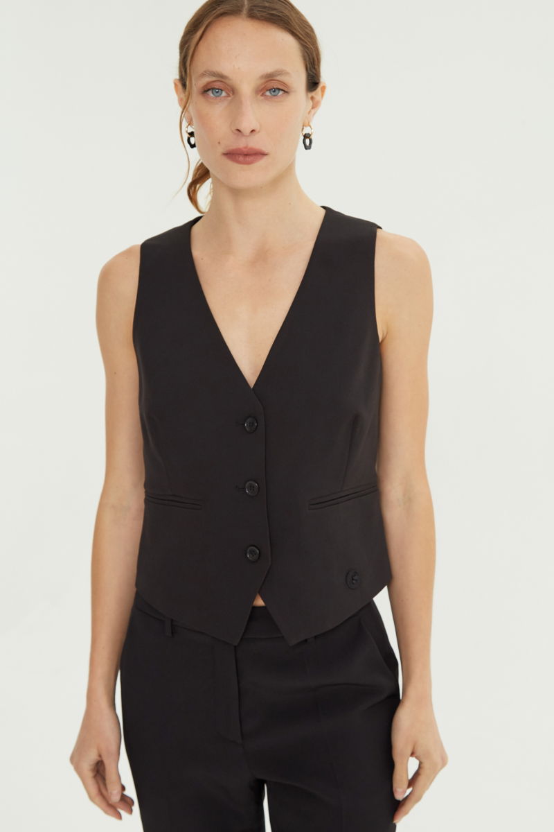 Chaleco negro sastrero largo a la cadera con botones a tono, bolsillos ojal y pinzas en frente y espalda. 
