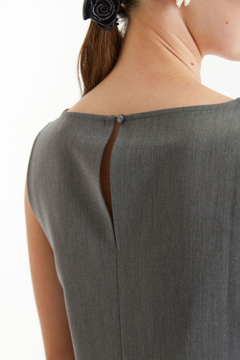 Blusa gris sastrera sin mangas con tablas en la cintura, herrajes metálicos y escote a la base del cuello, larga a la cadera. 