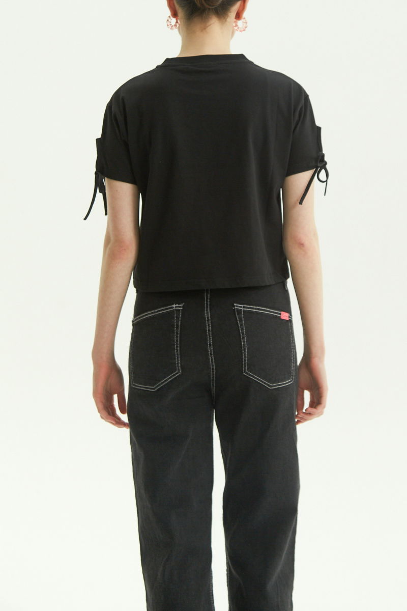 Remera negra suelta y crop de algodón estampada con lazos en las mangas para atar en moño.
