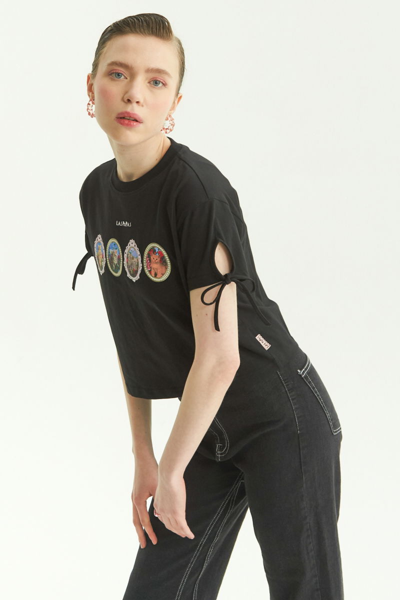 Remera negra suelta y crop de algodón estampada con lazos en las mangas para atar en moño.
