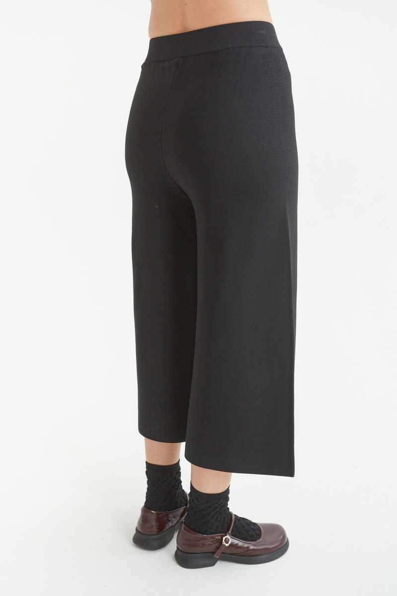 Pantalón negro tejido tiro alto y de calce recto con cintura elástica, piernas anchas y largo por arriba de los tobillos. 