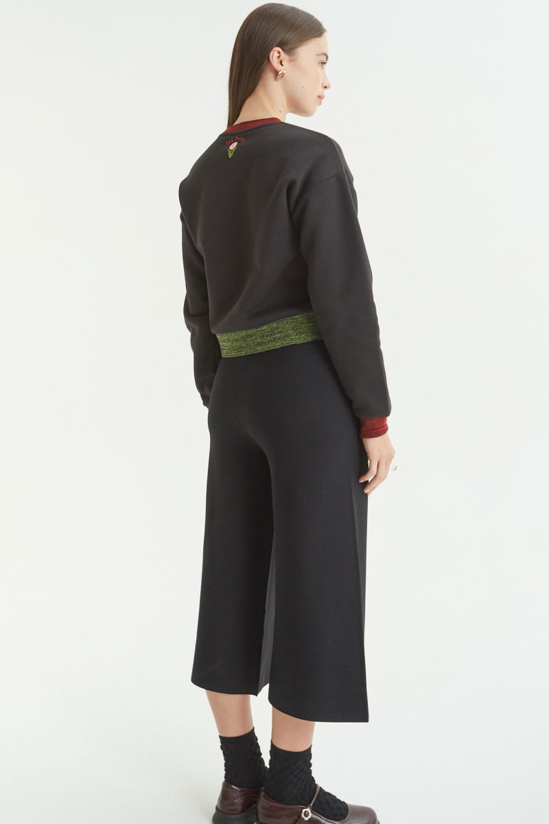 Pantalón negro tejido tiro alto y de calce recto con cintura elástica, piernas anchas y largo por arriba de los tobillos. 