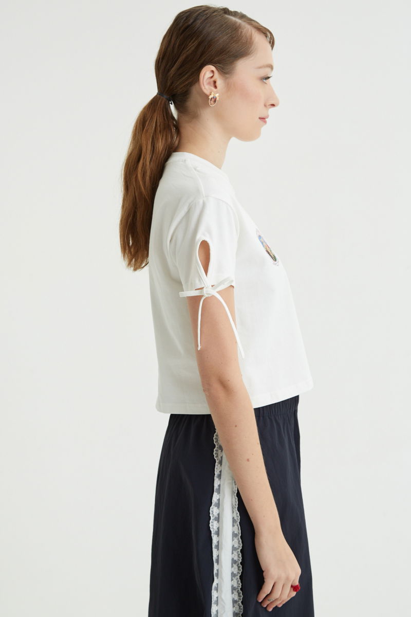 Remera blanca suelta y crop de algodón estampada con lazos en las mangas para atar en moño.
