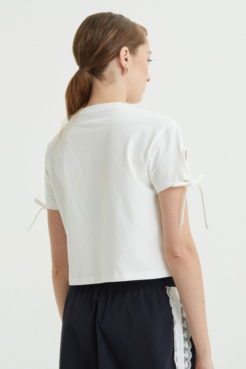 Remera blanca suelta y crop de algodón estampada con lazos en las mangas para atar en moño.
