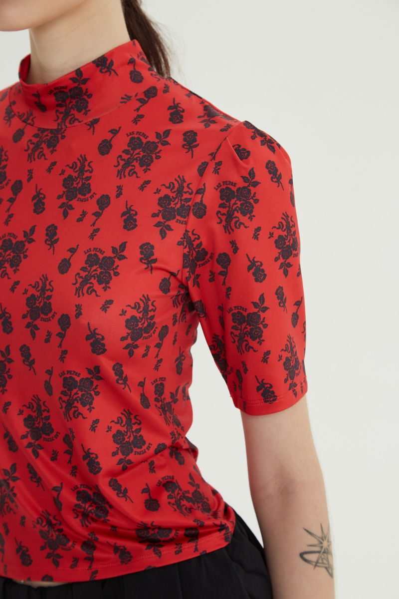 Remera roja entallada y larga a la cadera con cuello semi polera y mangas ¾ con frunces, estampada con print de rosas. 