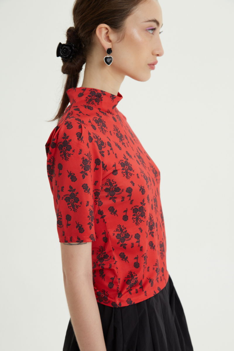 Remera roja entallada y larga a la cadera con cuello semi polera y mangas ¾ con frunces, estampada con print de rosas. 