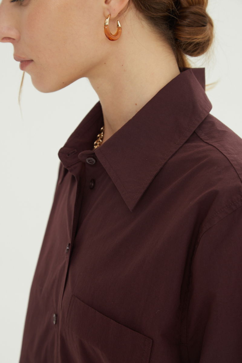 Camisa uva oversize de poplín de algodón larga por debajo de la cadera con bolsillo aplicado al frente, tabla en la espalda y botones a tono.