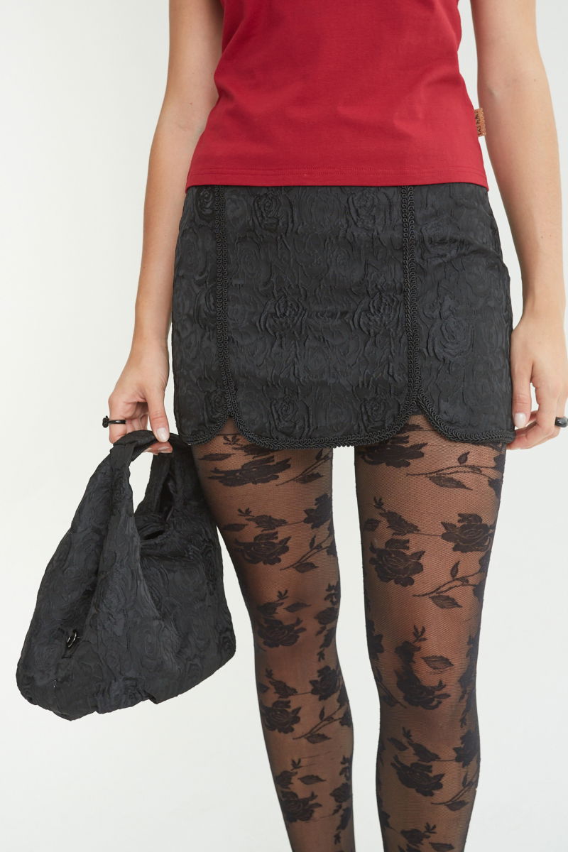 Mini falda negra recta y tiro bajo de brocato con tajos al frente con pasamanería. 
