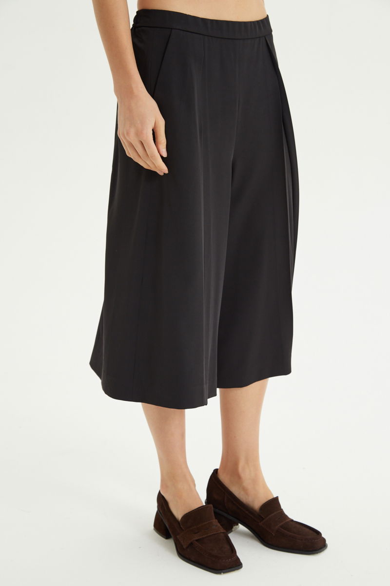 Bermuda negra sastrera tiro medio con piernas anchas hasta la rodilla, cintura trasera con elástico, tablas y bolsillos laterales. 