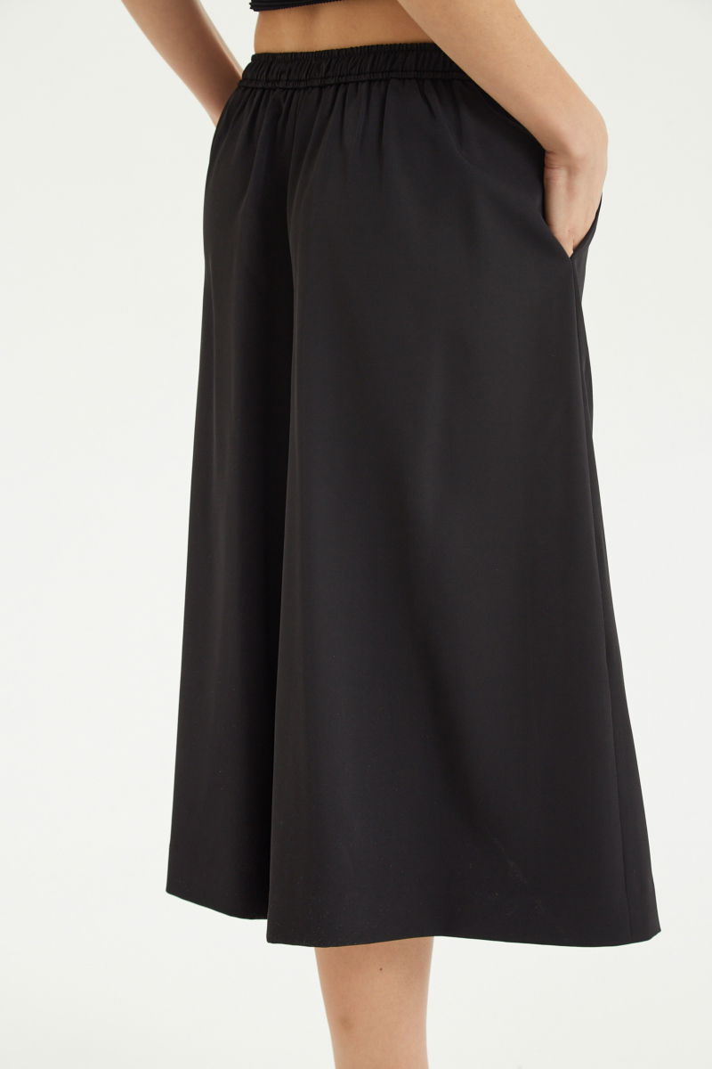 Bermuda negra sastrera tiro medio con piernas anchas hasta la rodilla, cintura trasera con elástico, tablas y bolsillos laterales. 