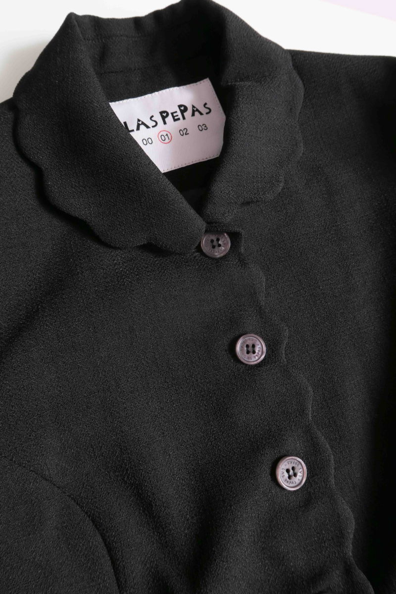 Blazer negro sastrero entallado con terminación ondulada y mangas princesa. 
