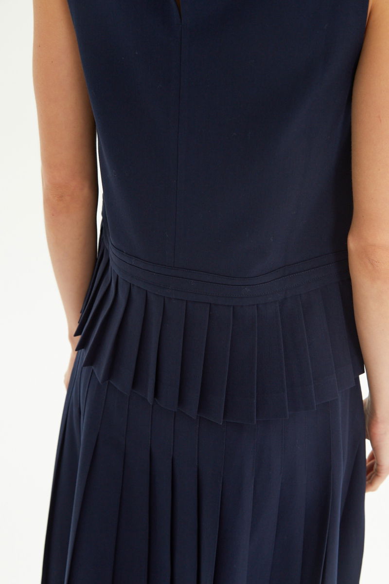 Blusa azul sastrera sin mangas con tablas en la cintura, herrajes metálicos y escote a la base del cuello, larga a la cadera. 