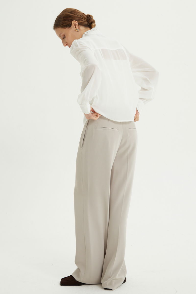 Camisa cruda de seda recta y larga a la cadera con cuello mao y volados en el cuello y la cartera, con frunces en los hombros y puños y botones a tono. 