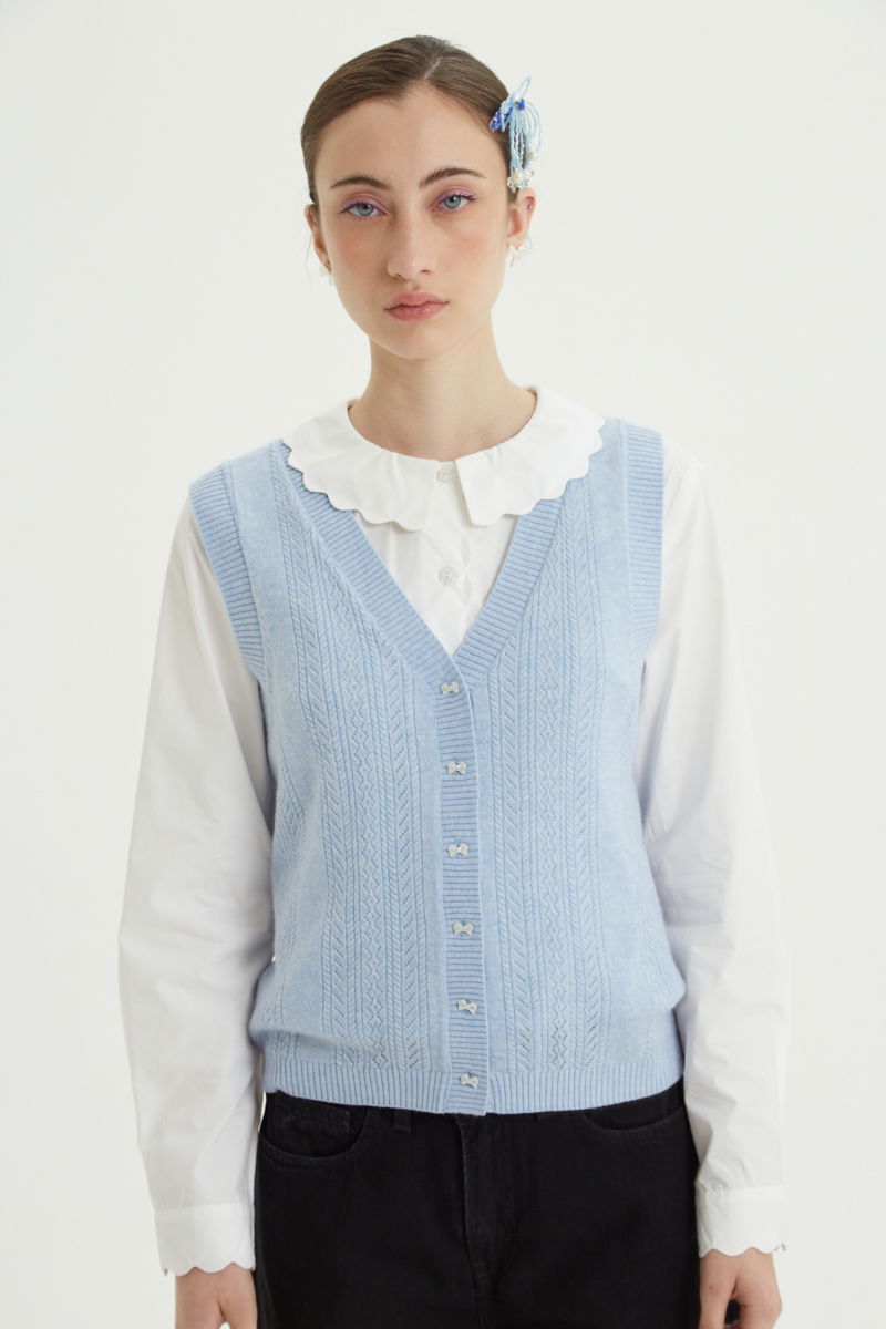 Camisa blanco de poplin de largo hasta la cadera con terminación en forma de onditas en cuello, puños y cartera y botones a tono en forma de flor. 