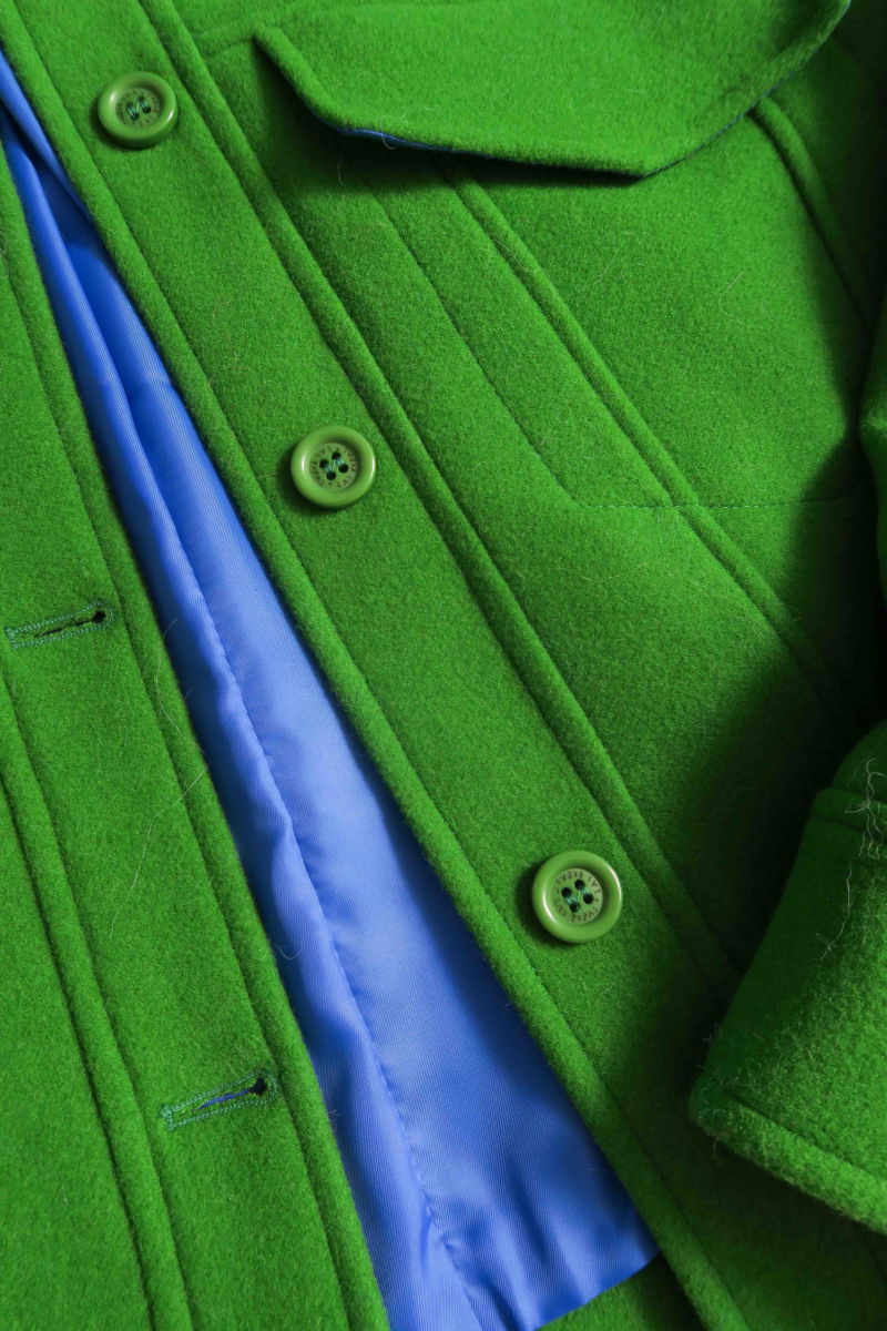 Campera verde de lana recta y larga hasta la cadera con sisas caídas, cuello en punta, botones a tono y bolsillos delanteros con solapa. 