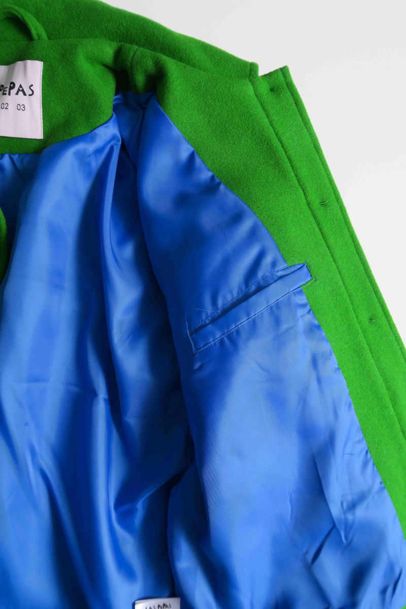 Campera verde de lana recta y larga hasta la cadera con sisas caídas, cuello en punta, botones a tono y bolsillos delanteros con solapa. 