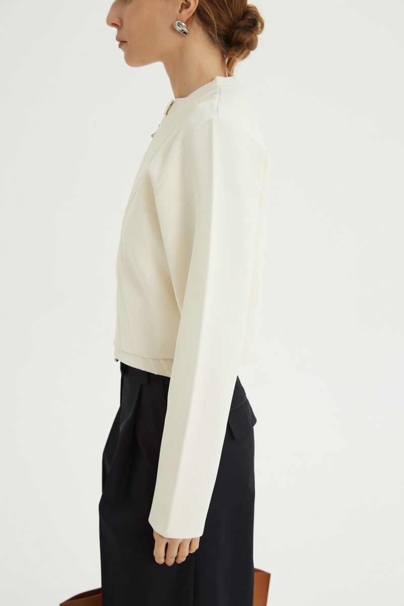 Campera crudo tejida estilo bomber larga a la cadera con cierre doble camino, cuello mao con broche snap, hombros anchos y terminación redondeada en el ruedo.