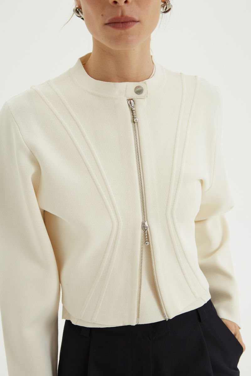 Campera crudo tejida estilo bomber larga a la cadera con cierre doble camino, cuello mao con broche snap, hombros anchos y terminación redondeada en el ruedo.