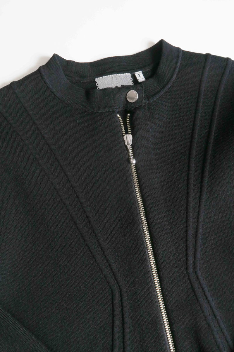 Campera negra tejida estilo bomber larga a la cadera con cierre doble camino, cuello mao con broche snap, hombros anchos y terminación redondeada en el ruedo.