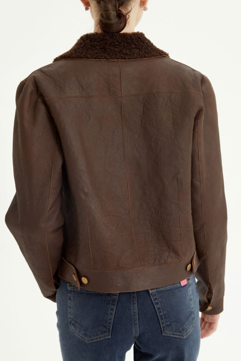 Campera de cuero marron con interior de pelo afelpado, recta y larga a la cadera con botones chatos metalicos y solapas frontales que simulan ser bolsillos. 