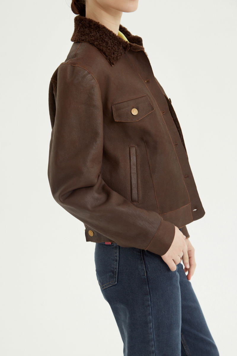 Campera de cuero marron con interior de pelo afelpado, recta y larga a la cadera con botones chatos metalicos y solapas frontales que simulan ser bolsillos. 