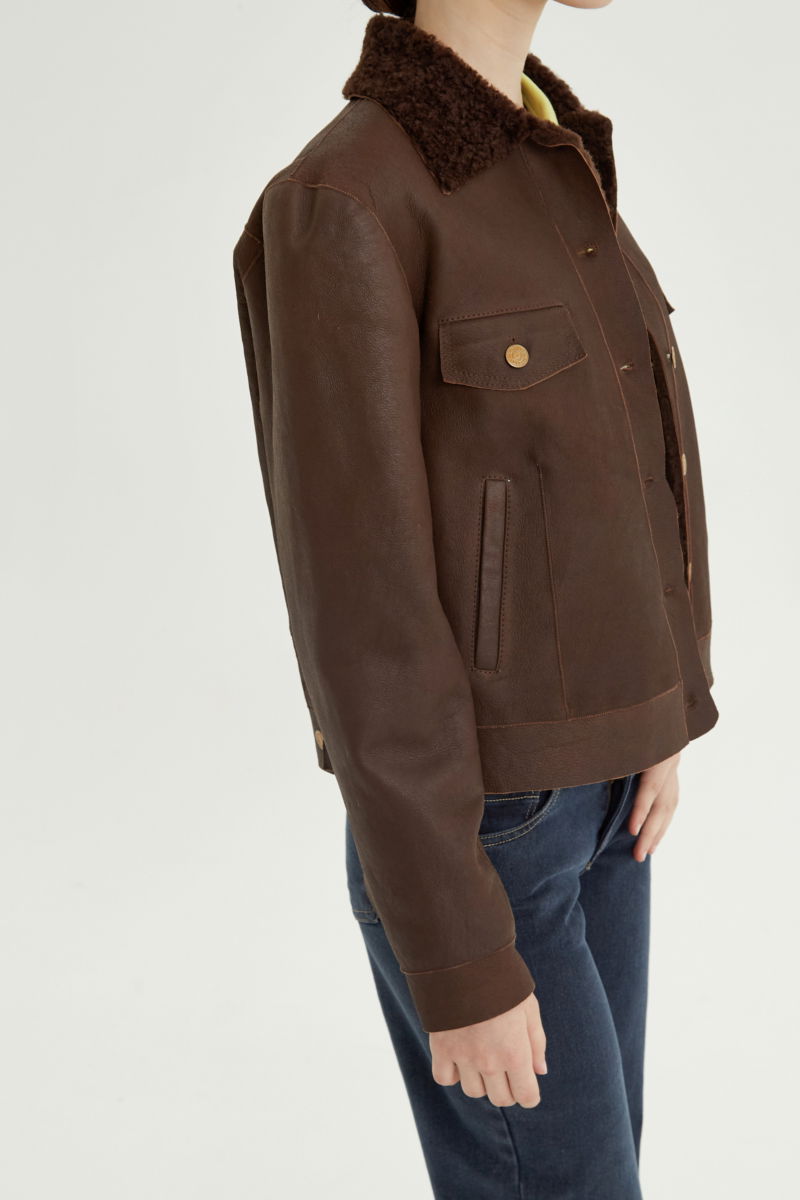 Campera de cuero marron con interior de pelo afelpado, recta y larga a la cadera con botones chatos metalicos y solapas frontales que simulan ser bolsillos. 