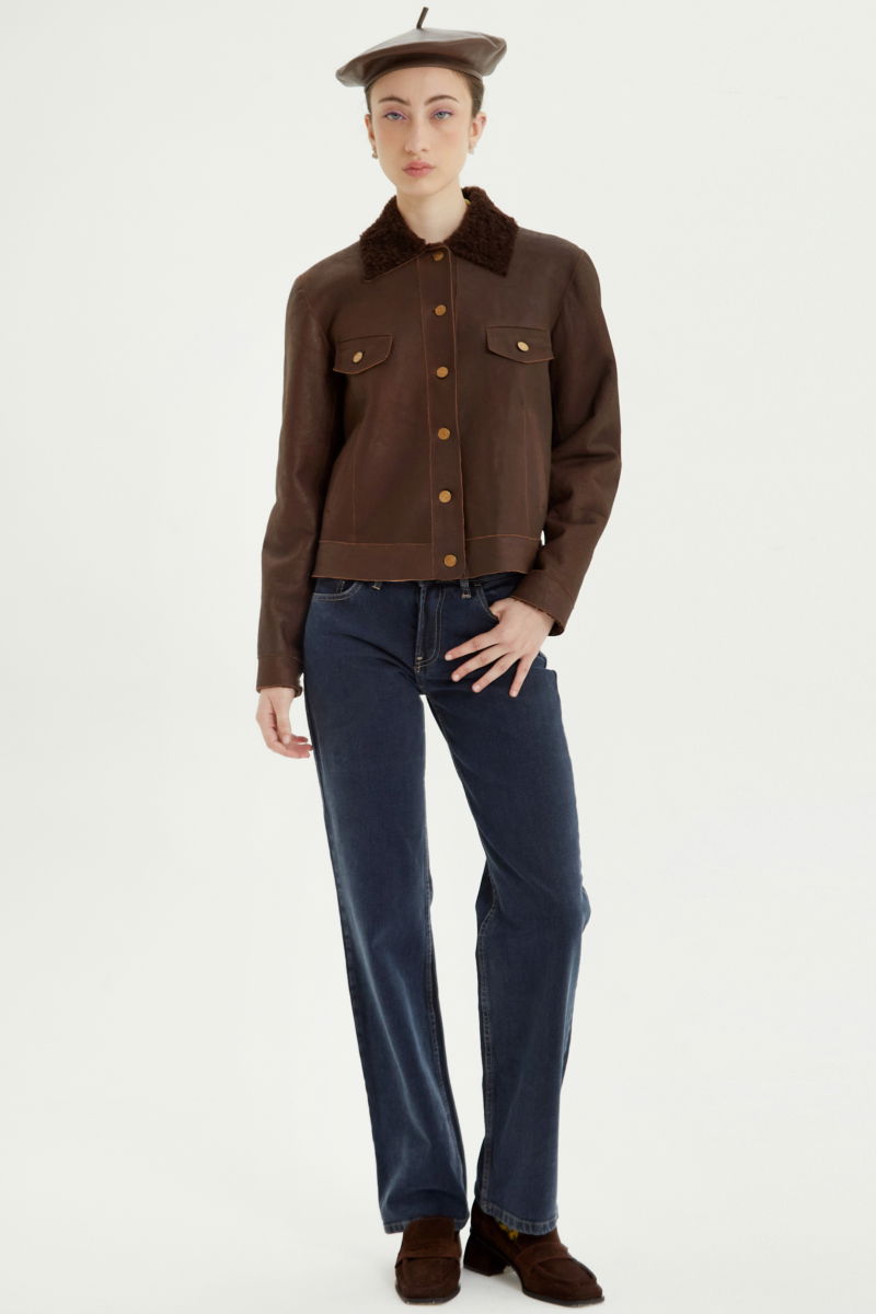 Campera de cuero marron con interior de pelo afelpado, recta y larga a la cadera con botones chatos metalicos y solapas frontales que simulan ser bolsillos. 