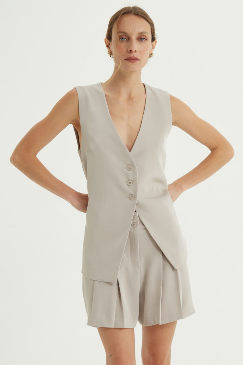 Short beige sastrero con pinzas delanteras, cintura ancha con presillas para cinturón y botones a tono, bolsillos laterales y bolsillos ojal traseros.
