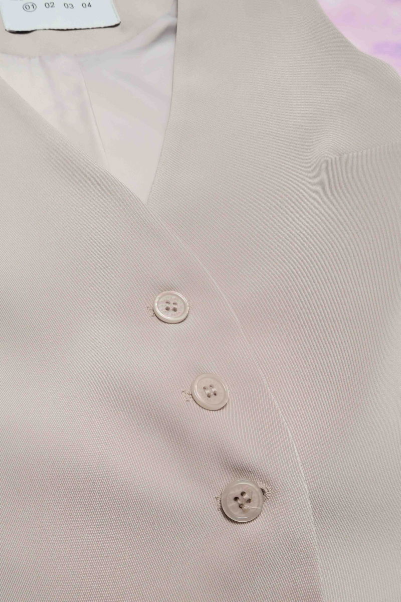 Chaleco sastrero beige con escote en V y largo a la cadera con botones a tono y lazo en la espalda. 